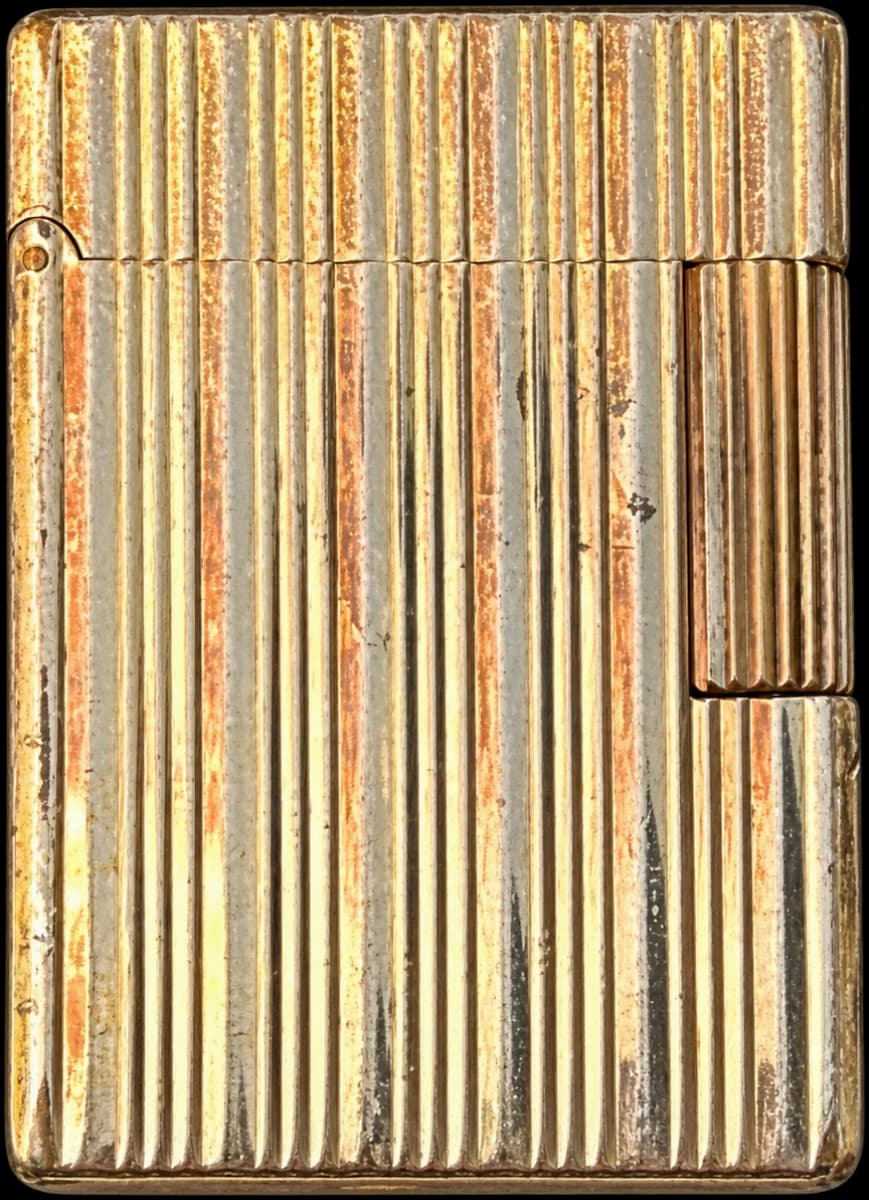 Closed rectangular gold-tone lighter with vertical fluting and visible patina